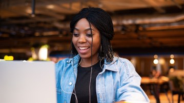 An African-American black woman smiles while looking at a laptop. Coworking for business and work, favorable price, good news for the student